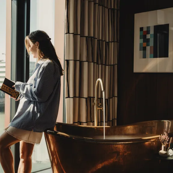 Woman leaning against Copper Bath tub in the Dean Docklands Suites