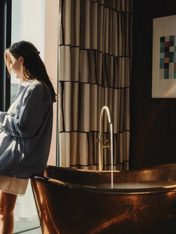 Woman leaning against Copper Bath tub in the Dean Docklands Suites